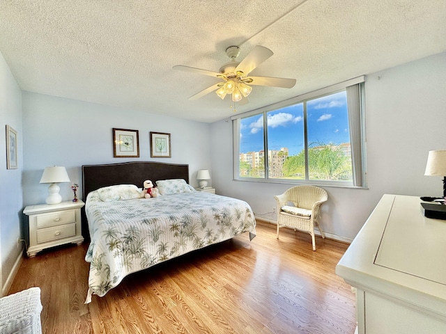 bedroom featuring baseboards, a ceiling fan, a textured ceiling, and wood finished floors