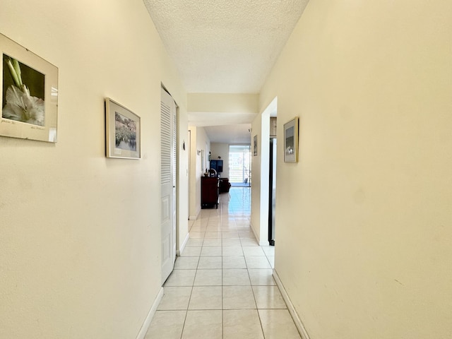 hallway featuring baseboards, a textured ceiling, and light tile patterned flooring