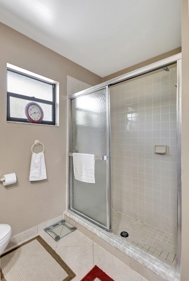 bathroom with tile patterned flooring, baseboards, a tile shower, and toilet
