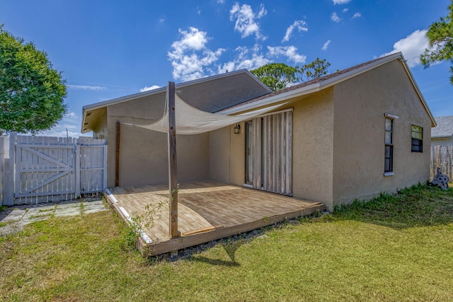 back of property with fence, stucco siding, a deck, a gate, and a lawn
