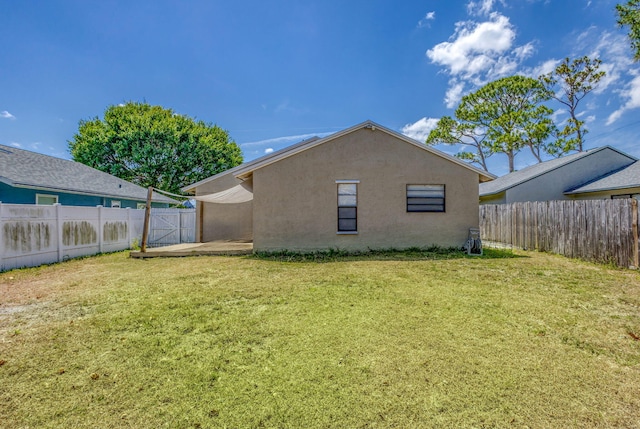 rear view of house with a fenced backyard, stucco siding, and a yard