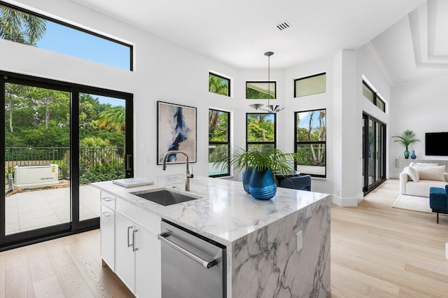 kitchen featuring hanging light fixtures, light wood-style flooring, dishwasher, a sink, and white cabinetry