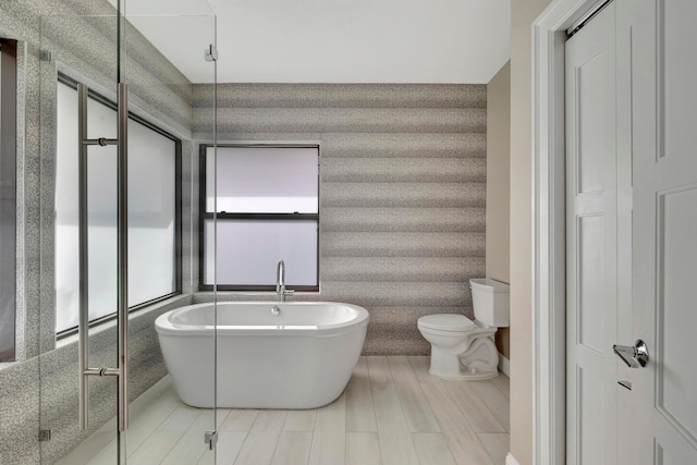 bathroom with a freestanding tub, toilet, and wallpapered walls