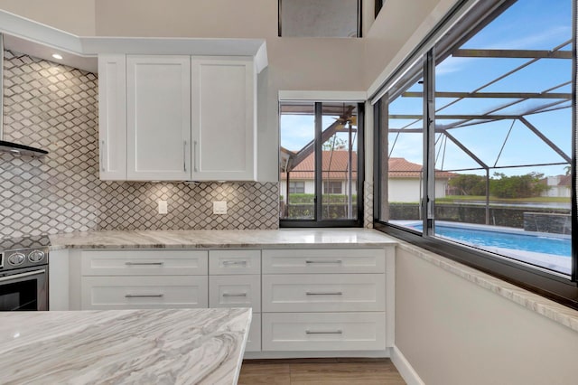 kitchen with baseboards, white cabinets, stainless steel electric stove, light stone counters, and backsplash