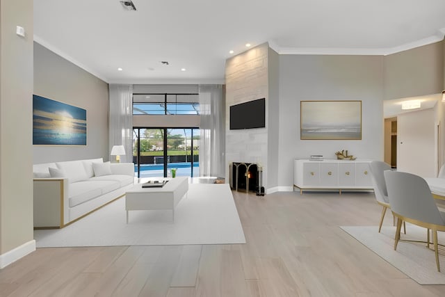 living area featuring a large fireplace, baseboards, ornamental molding, and light wood-style floors