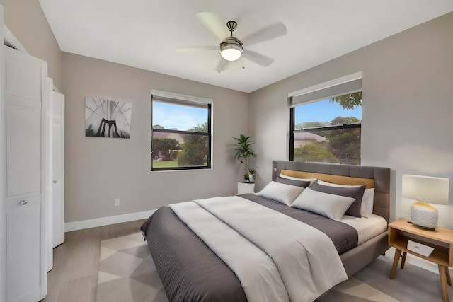 bedroom with baseboards, light wood-style flooring, ceiling fan, and multiple windows