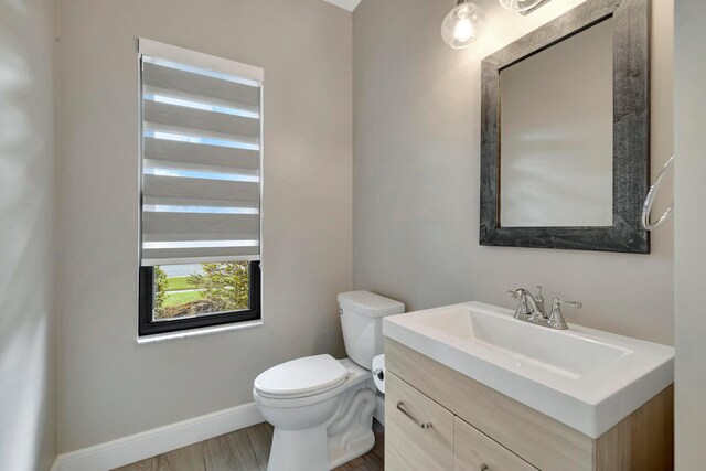 half bathroom featuring toilet, baseboards, and vanity