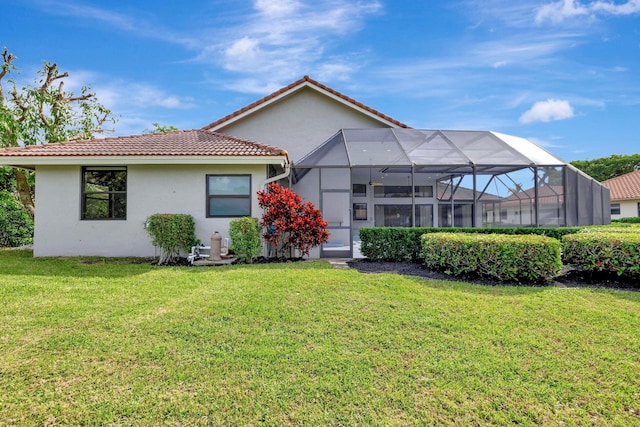 back of property featuring glass enclosure, stucco siding, a yard, and a tile roof