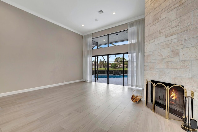 unfurnished living room with visible vents, a fireplace, wood finished floors, baseboards, and ornamental molding