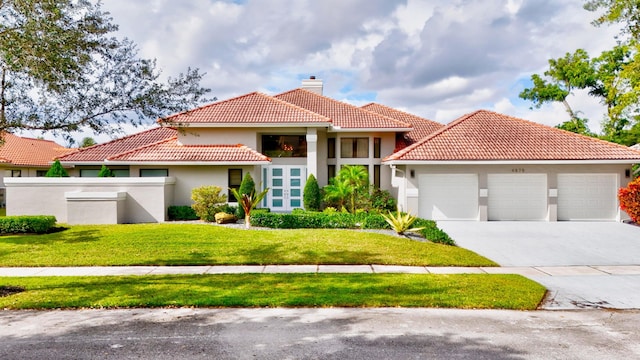 mediterranean / spanish house featuring a front lawn, a garage, stucco siding, a chimney, and concrete driveway