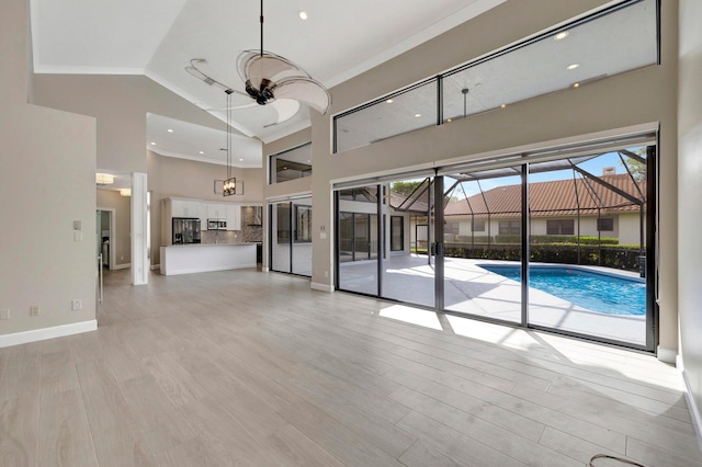 unfurnished living room with ceiling fan, baseboards, a high ceiling, and light wood-style flooring