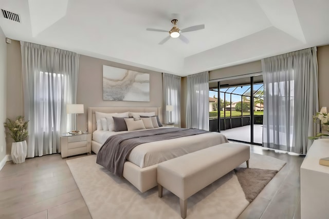 bedroom with visible vents, access to exterior, ceiling fan, light wood-type flooring, and a raised ceiling