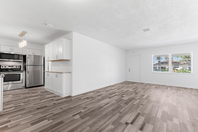 9603 NW 72nd Mnr, Tamarac, FL 33321 - unfurnished living room featuring a textured ceiling, visible vents, light wood-type flooring, baseboards, and a notable chandelier