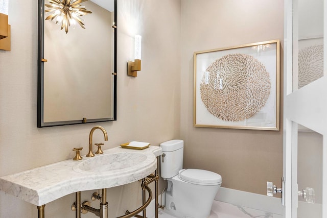 half bathroom with toilet, marble finish floors, baseboards, and a sink