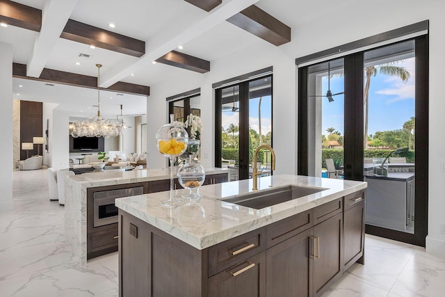 kitchen with a sink, a kitchen island with sink, beam ceiling, light marble finish floors, and french doors
