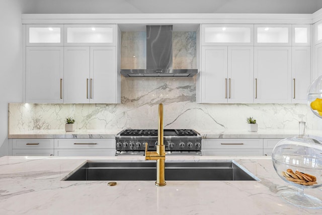kitchen featuring wall chimney range hood, stainless steel range, tasteful backsplash, light stone countertops, and white cabinets