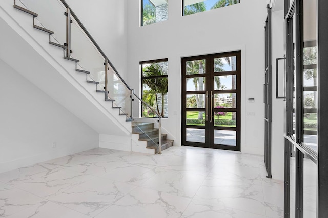 foyer featuring healthy amount of natural light, stairway, a towering ceiling, light marble finish floors, and baseboards