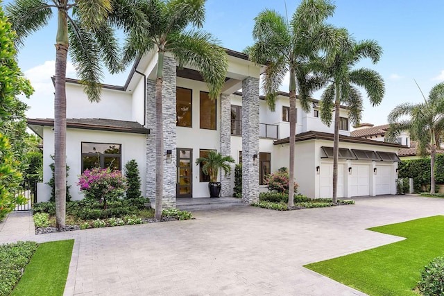 modern home with stucco siding, decorative driveway, a balcony, and stone siding