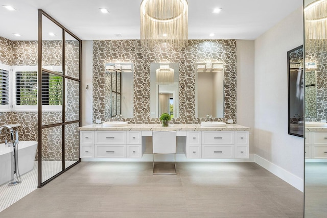 full bath with a soaking tub, double vanity, wallpapered walls, and baseboards
