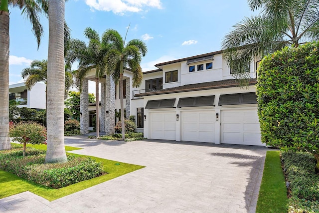 contemporary house featuring stucco siding, an attached garage, and decorative driveway