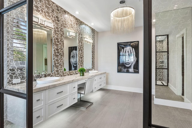bathroom with baseboards, double vanity, and wallpapered walls