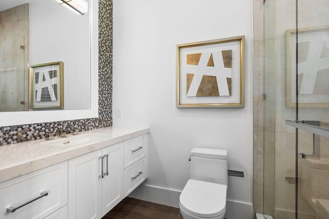 bathroom with toilet, wood finished floors, vanity, a stall shower, and backsplash