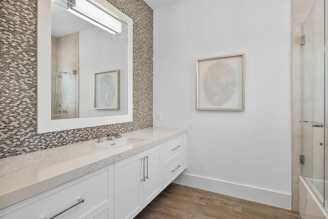 bathroom with vanity, backsplash, wood finished floors, baseboards, and combined bath / shower with glass door