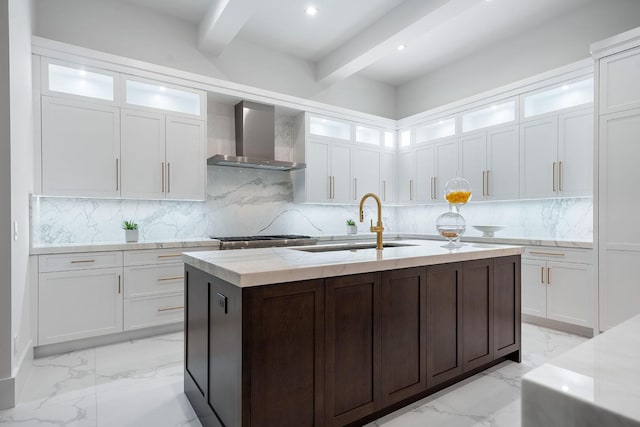 kitchen with wall chimney exhaust hood, a sink, light marble finish floors, beam ceiling, and white cabinets