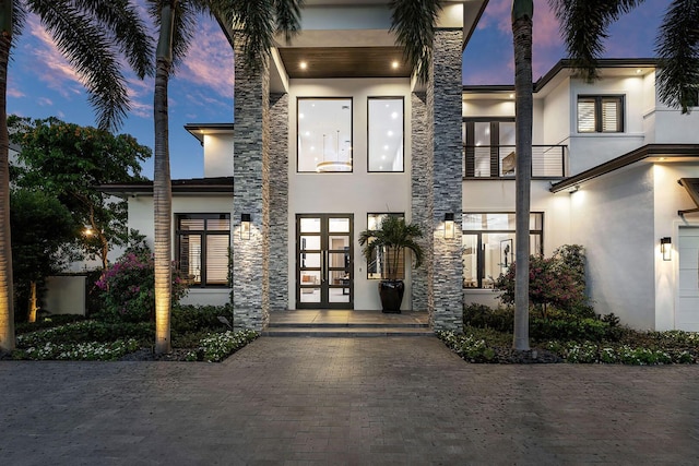 view of front facade featuring stucco siding, french doors, and stone siding