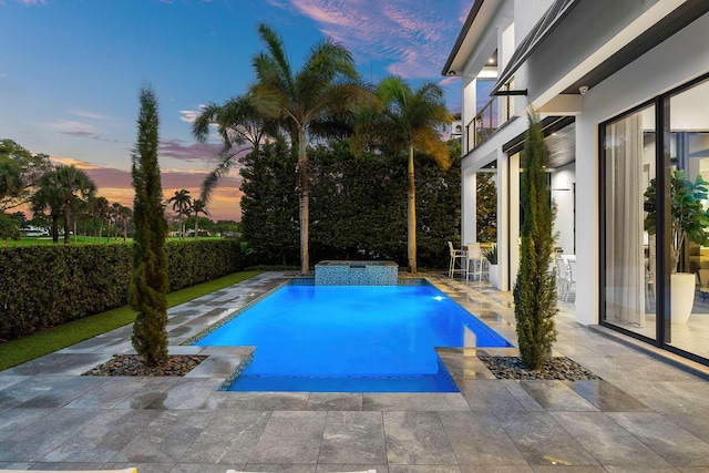 pool at dusk featuring a patio area and a pool with connected hot tub