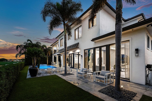 back of property at dusk with stucco siding, a patio area, an outdoor pool, and a yard