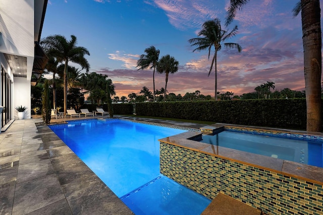 pool at dusk featuring a patio, a pool with connected hot tub, and fence