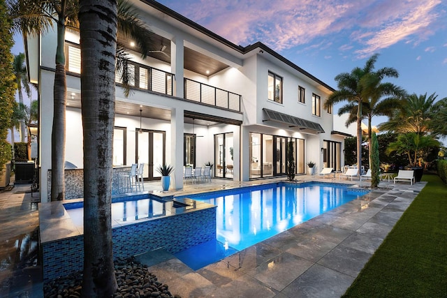 pool at dusk featuring a patio area, a ceiling fan, and a pool with connected hot tub