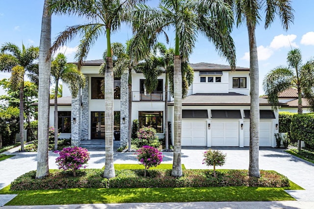 view of front of property featuring an attached garage, stucco siding, a balcony, and decorative driveway