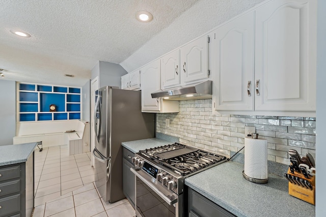 kitchen with light tile patterned flooring, a textured ceiling, under cabinet range hood, white cabinets, and stainless steel appliances