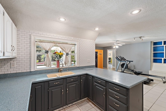 kitchen with a ceiling fan, a textured ceiling, a sink, white cabinets, and a peninsula