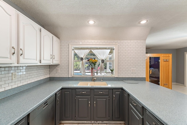 kitchen featuring decorative backsplash, a textured ceiling, stainless steel dishwasher, a sink, and white cabinetry
