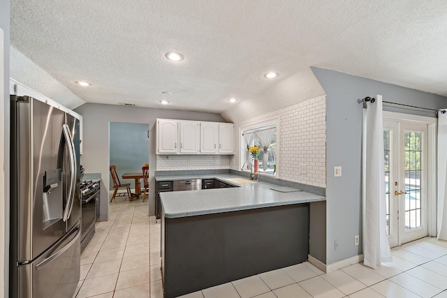 kitchen with a textured ceiling, gas stove, a peninsula, lofted ceiling, and stainless steel fridge