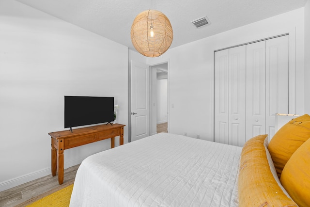 bedroom with visible vents, light wood-style flooring, baseboards, and a closet