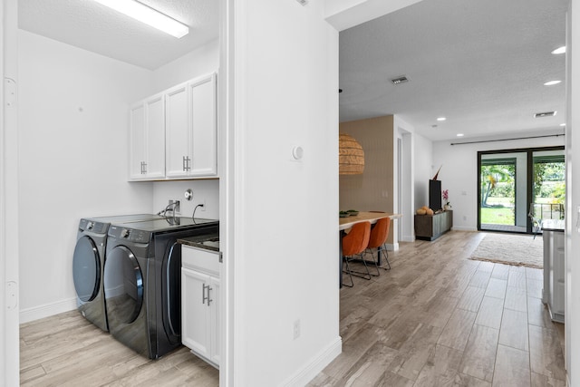 clothes washing area with a textured ceiling, cabinet space, baseboards, light wood-style flooring, and washer and clothes dryer