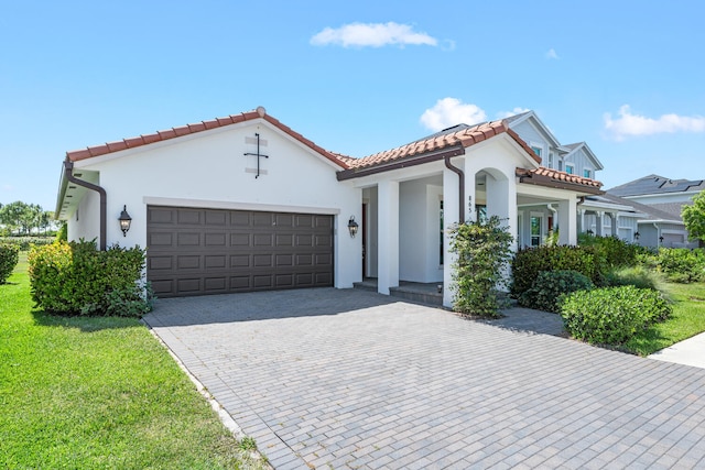 mediterranean / spanish-style home featuring an attached garage, a tile roof, stucco siding, covered porch, and driveway