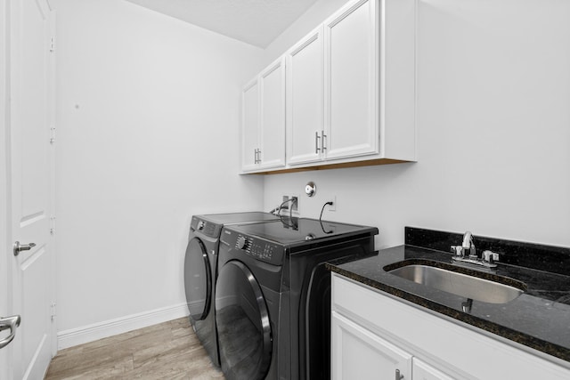 laundry area with washing machine and dryer, light wood-type flooring, cabinet space, a sink, and baseboards