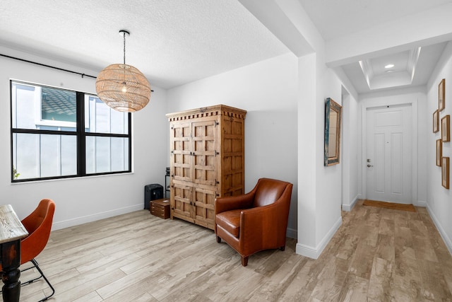 interior space with baseboards, light wood-type flooring, a textured ceiling, and a raised ceiling