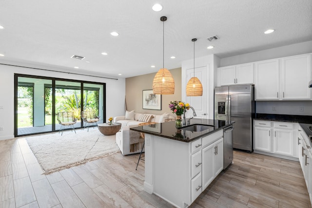 kitchen featuring visible vents, appliances with stainless steel finishes, a sink, open floor plan, and white cabinetry