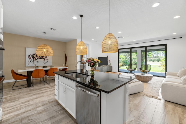 kitchen featuring stainless steel dishwasher, white cabinetry, open floor plan, and a sink