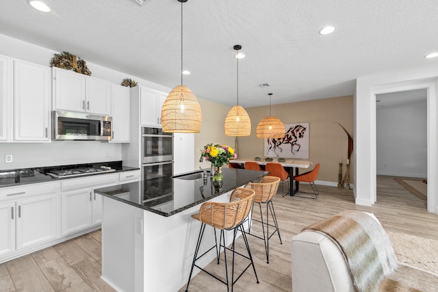 kitchen with light wood-type flooring, a textured ceiling, appliances with stainless steel finishes, and a breakfast bar area