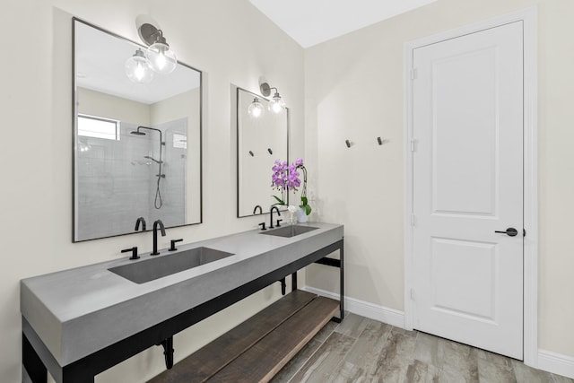 full bathroom with double vanity, wood finished floors, a sink, baseboards, and tiled shower