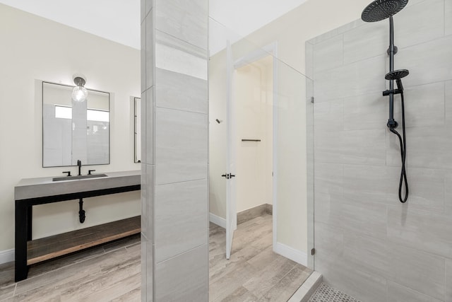 full bath with vanity, baseboards, wood finished floors, and tiled shower