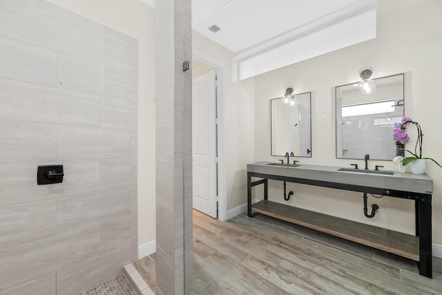 bathroom with a sink, tiled shower, wood finished floors, and visible vents