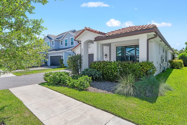 mediterranean / spanish home featuring decorative driveway, stucco siding, a tiled roof, and a front yard
